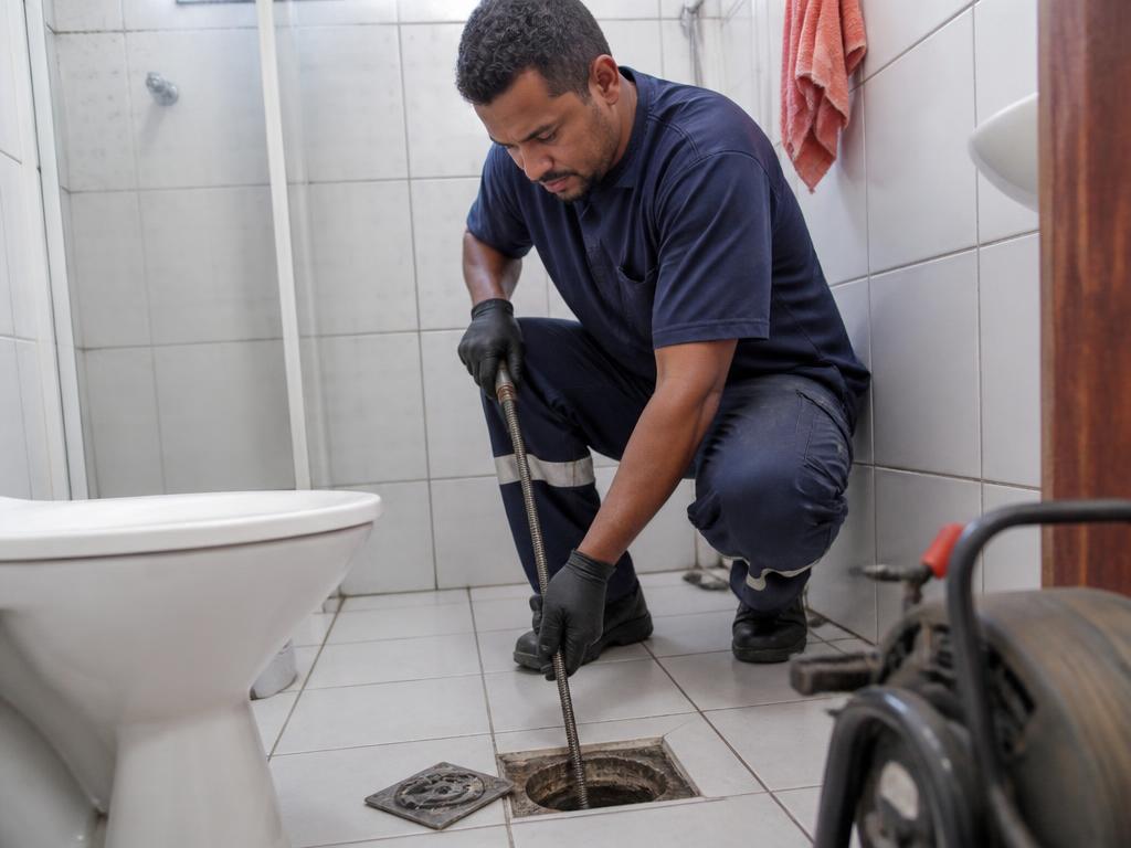 Profissional realizando desentupimento de ralo em banheiro residencial